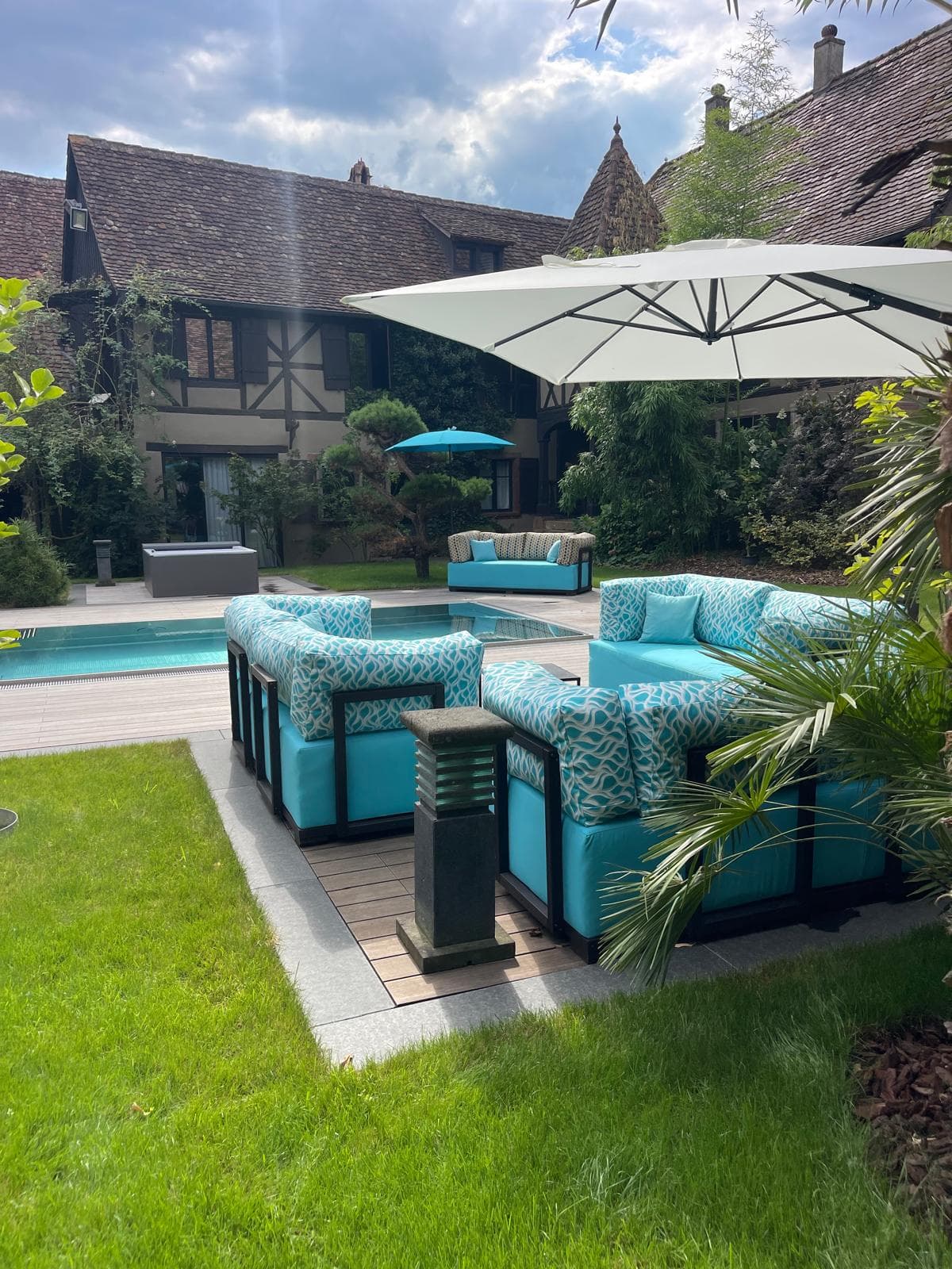 Piscine extérieure avec canapés turquoise face à une maison à colombages