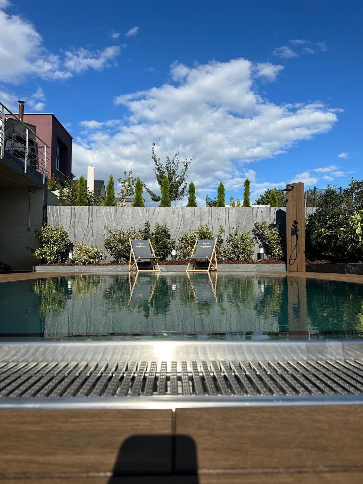 Piscine inox extérieure avec chaises longues face à un mur de pierre